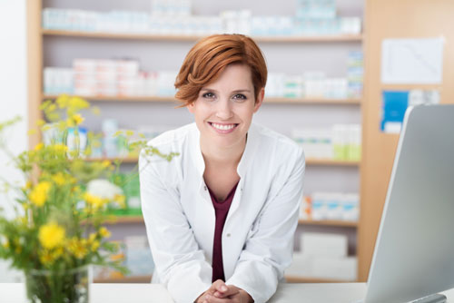 A woman wearing a medical gown leans over the counter in a pharmacy